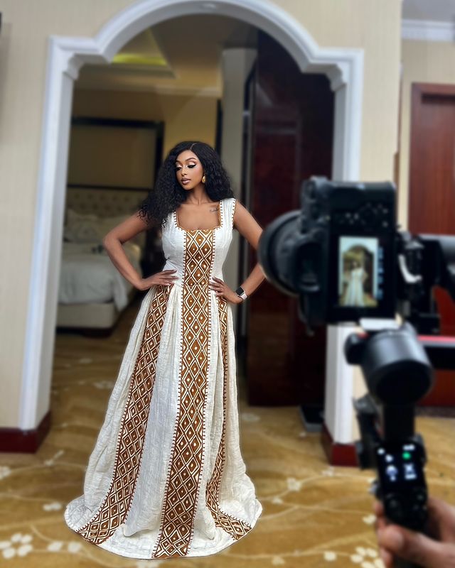 Woman in a white and gold patterned dress being filmed by a camera.