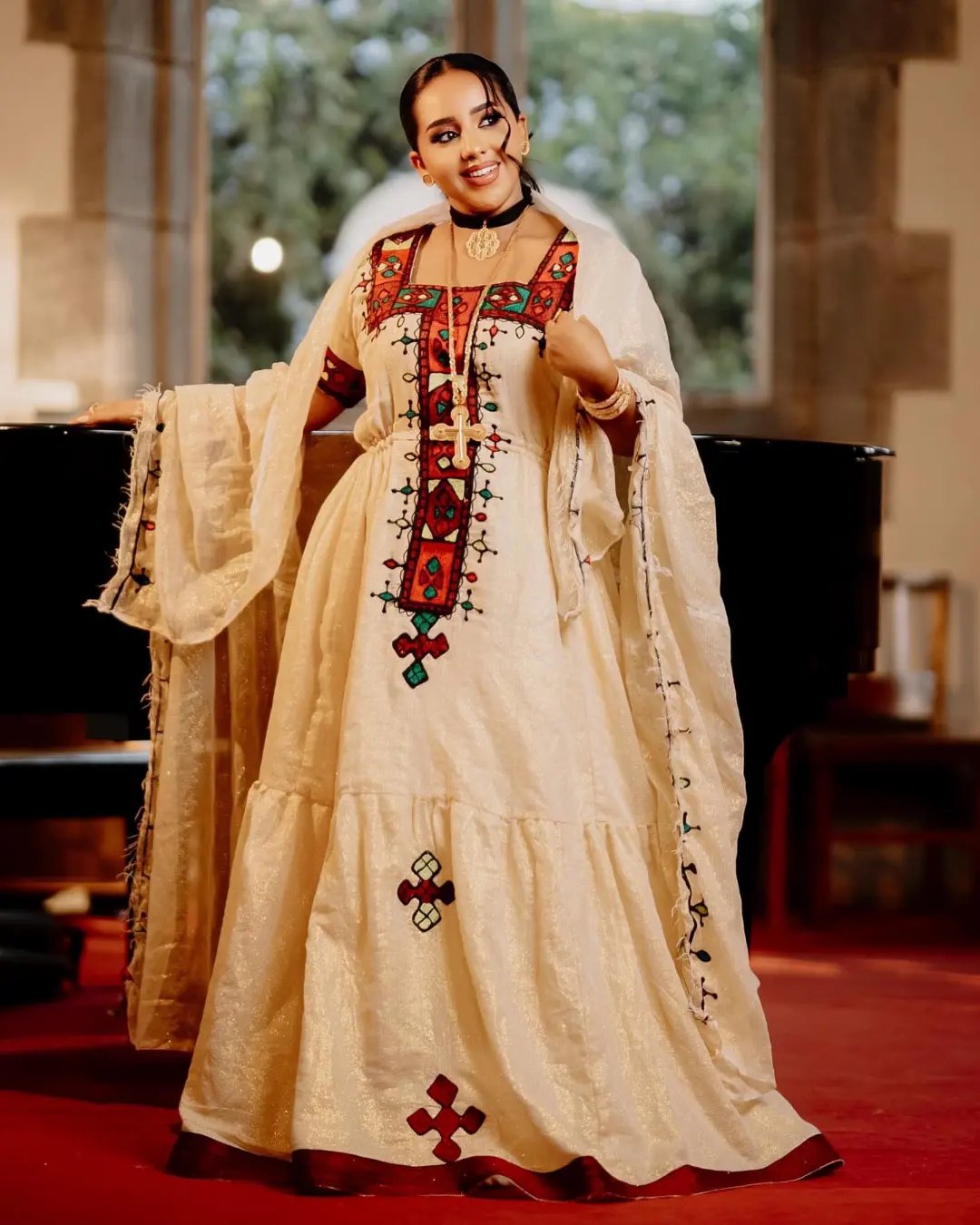 Woman in a traditional embroidered dress standing in a room with a piano.