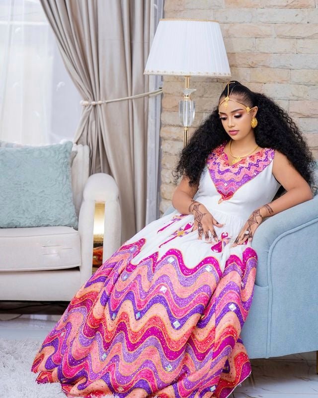 Woman in a colorful dress sitting on a couch in a living room.