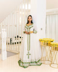 Woman in a white and green dress standing in a bright, elegant interior setting.