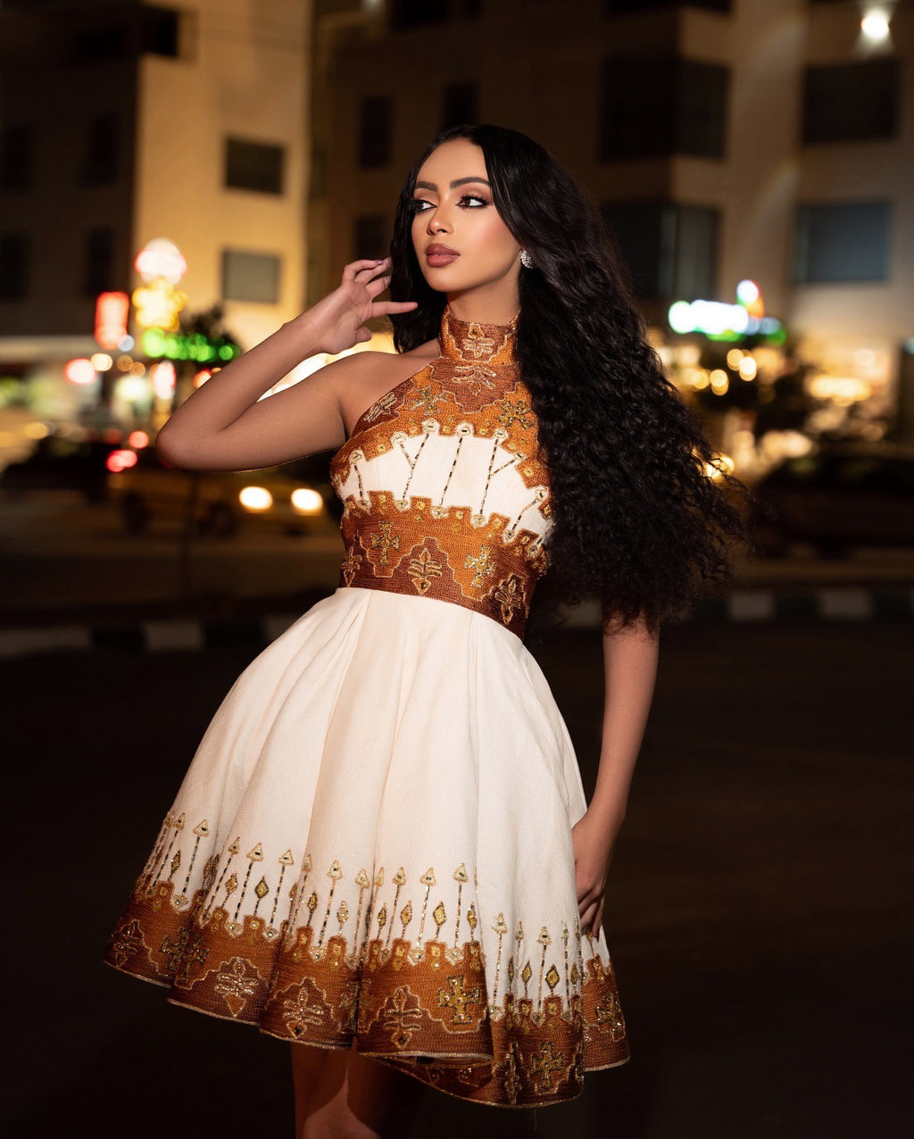 Woman wearing a traditional outfit with intricate patterns in an urban night setting.
