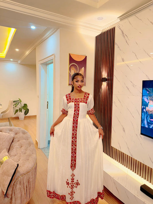 Woman in a white dress with red embroidery standing in a modern living room.