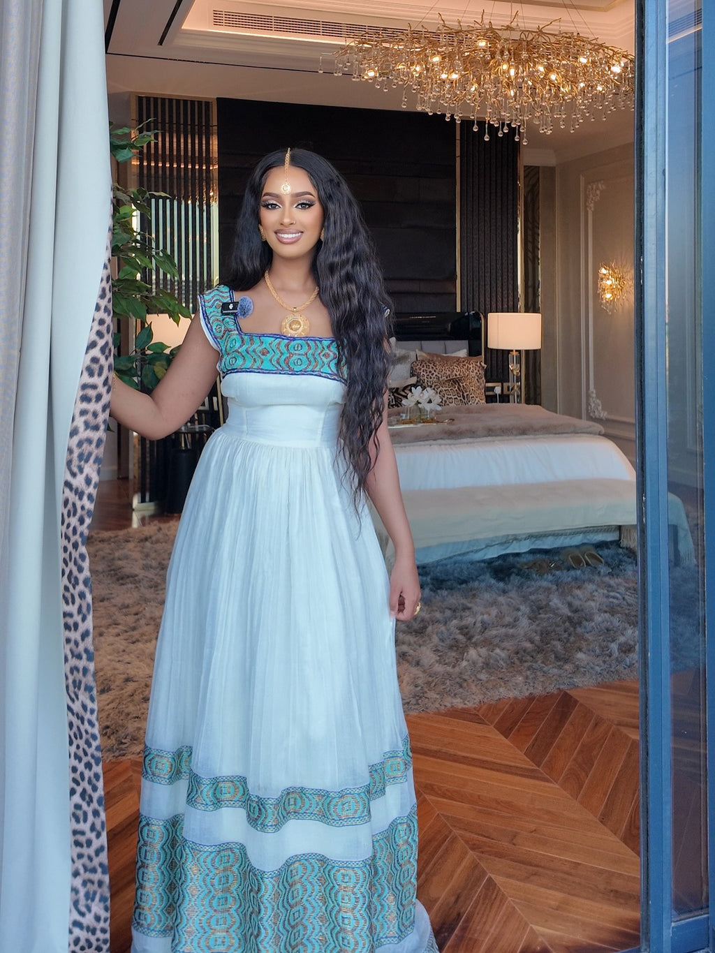 Woman in a light blue dress with green accents standing in a luxurious room.