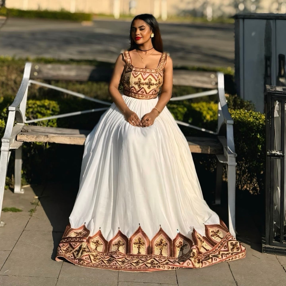 Woman wearing a traditional outfit with a white skirt and patterned top outdoors.