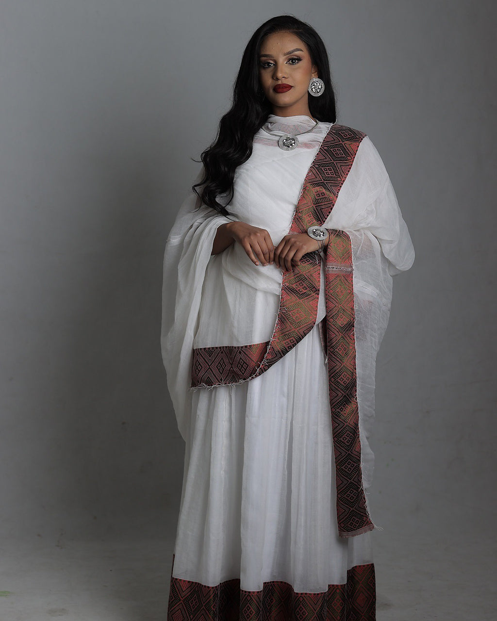 Woman wearing a white traditional outfit with a red and gold sash on a gray background