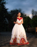 Woman in a white and red dress with intricate patterns standing outdoors.