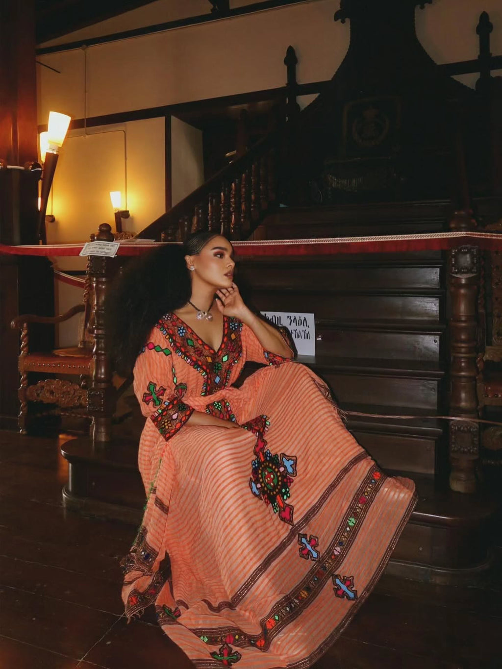 Woman in a traditional outfit sitting on a staircase in a dimly lit room.