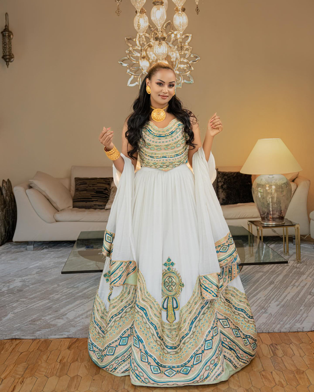 Woman in a traditional outfit standing in a decorated room with a chandelier and lamp.