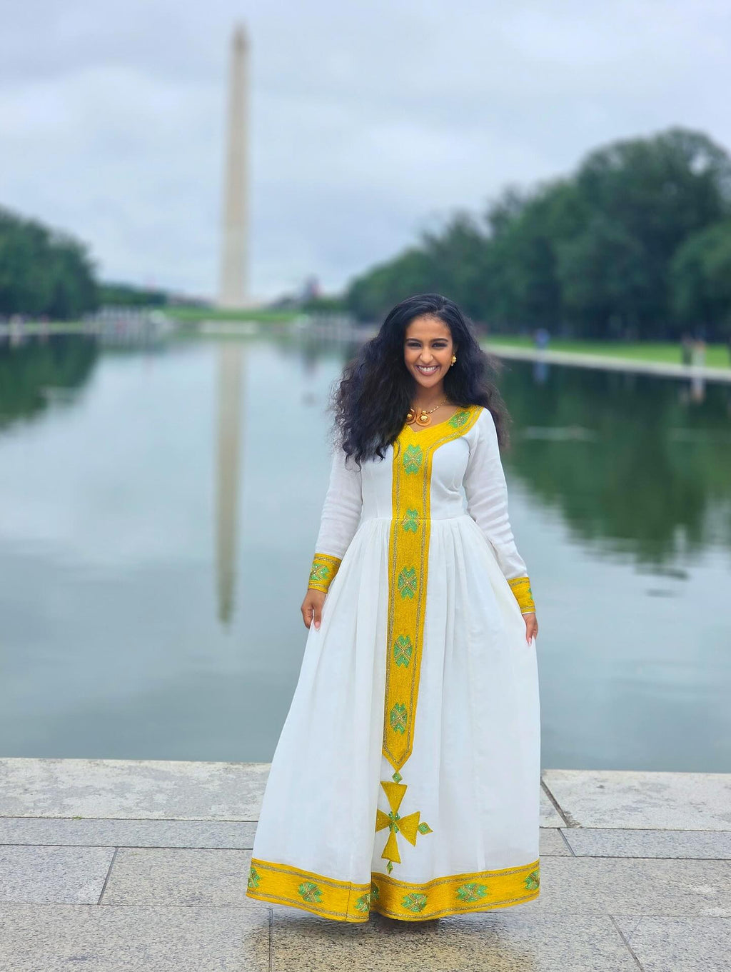 Woman in a white and yellow dress standing by a body of water with a monument in the background