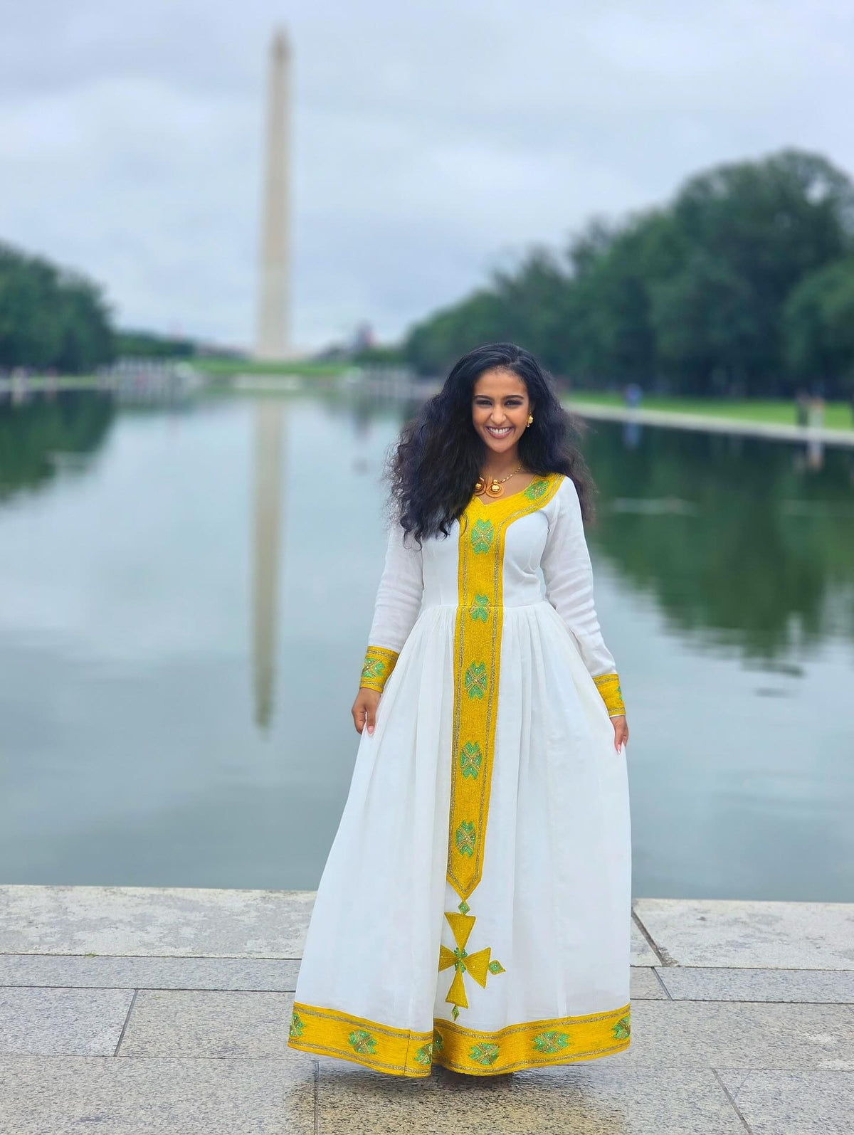 Woman in a white and yellow dress standing by a body of water with a monument in the background