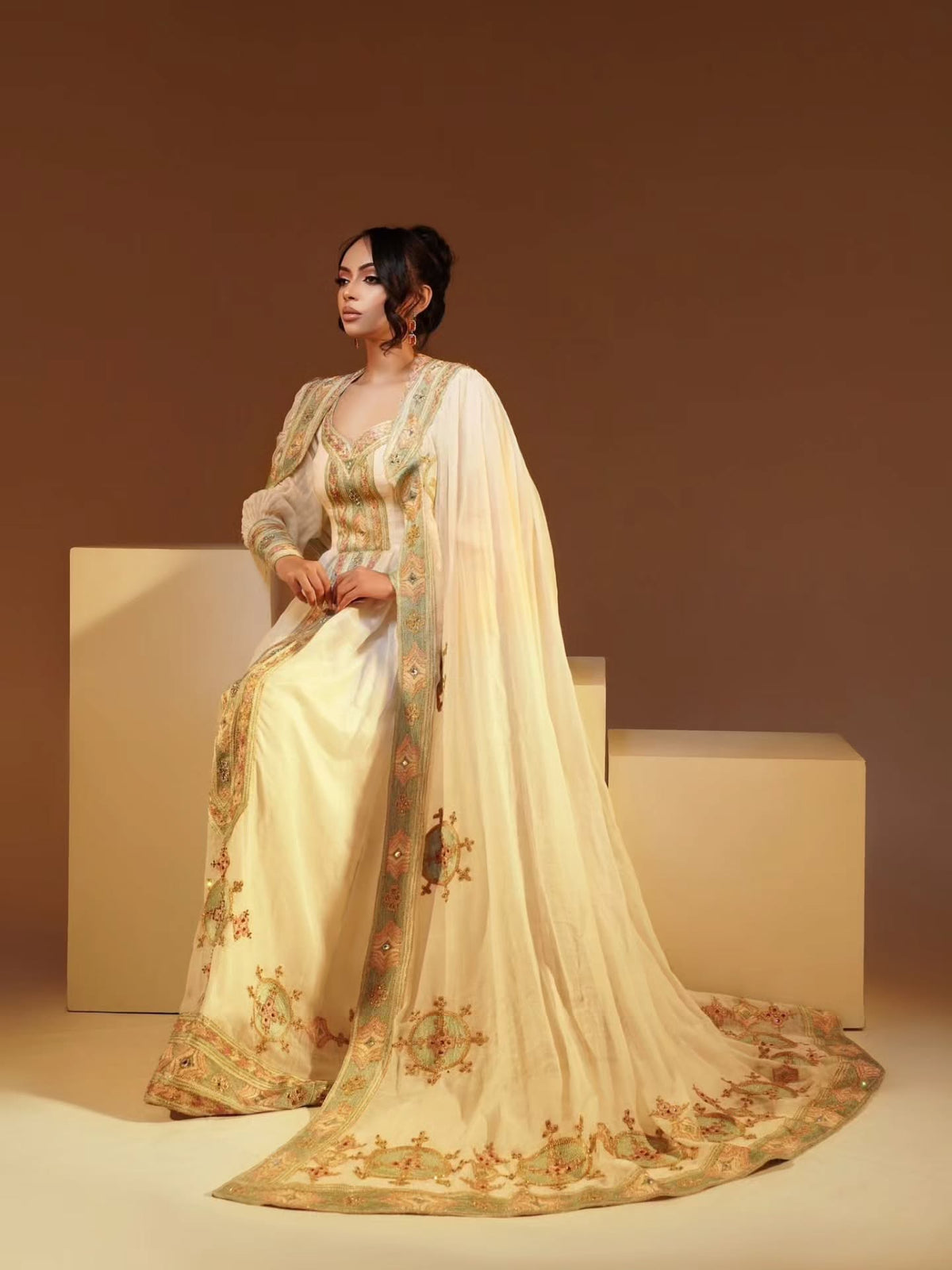 Woman in a traditional embroidered outfit sitting on a beige block against a brown background
