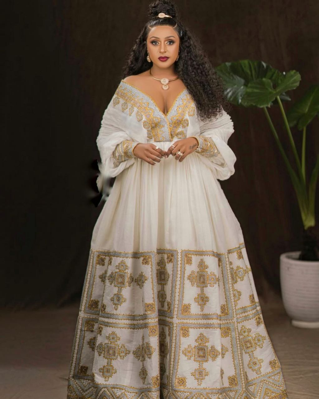Woman wearing a white dress with gold embroidery in a dark setting
