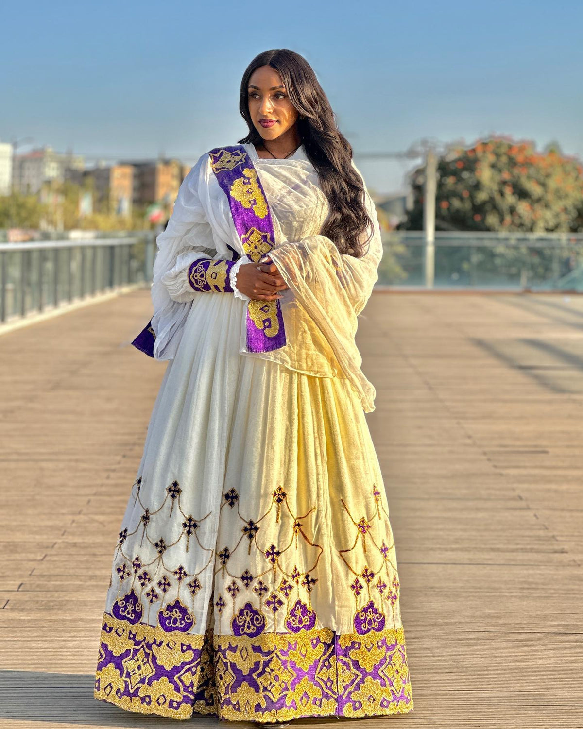 Woman in a traditional outfit with white, yellow, and purple colors on a wooden deck.
