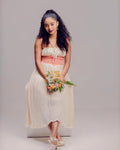 Woman in a white and pink dress holding flowers against a plain background