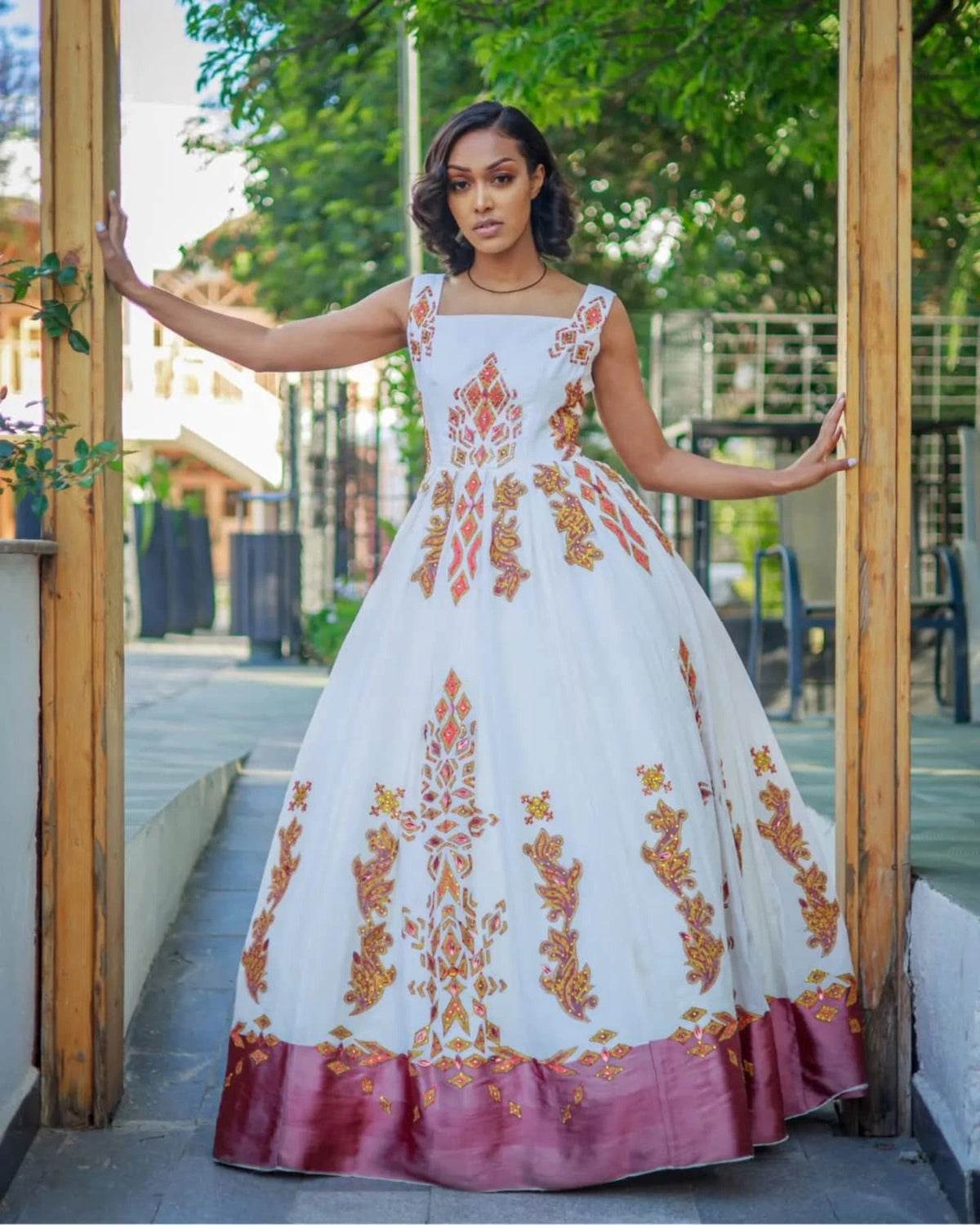 Woman in a white dress with orange floral patterns standing in front of a wooden door.