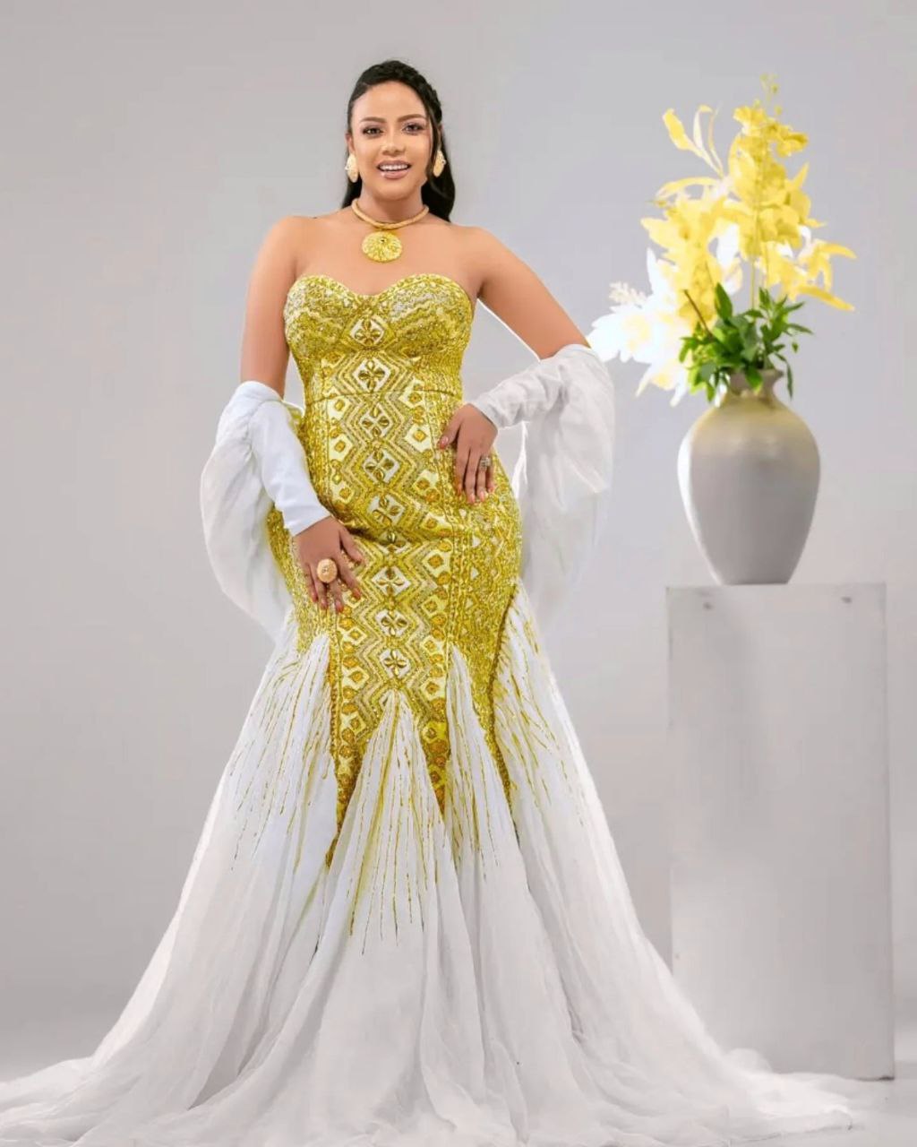 Woman in a yellow and white dress with a vase of flowers in the background