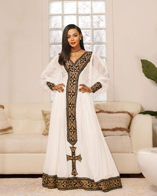 Woman wearing a white dress with black embroidery in a living room setting
