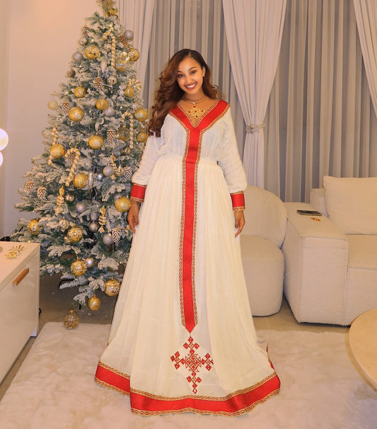 Woman in a white and red dress standing in a living room with a decorated Christmas tree.