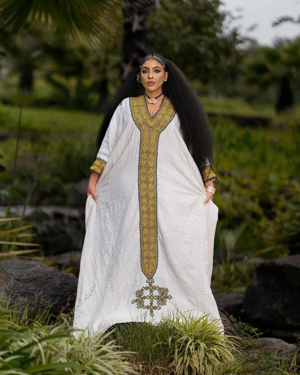 Woman in a white dress with gold embroidery standing in a natural setting